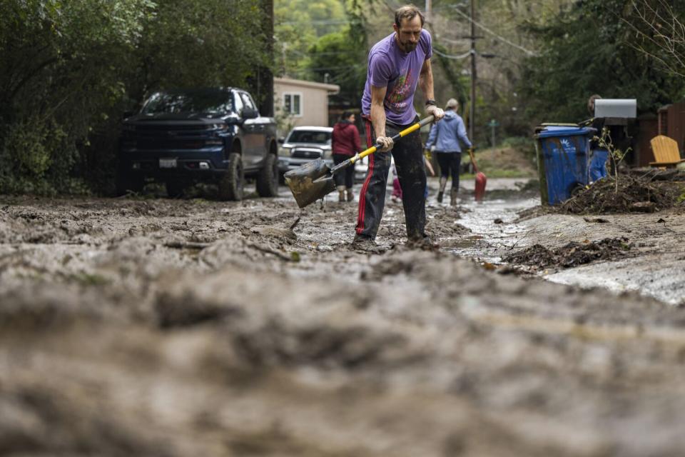 In the center of the frame man shovels mud while two other people walk with shovels in the distance.