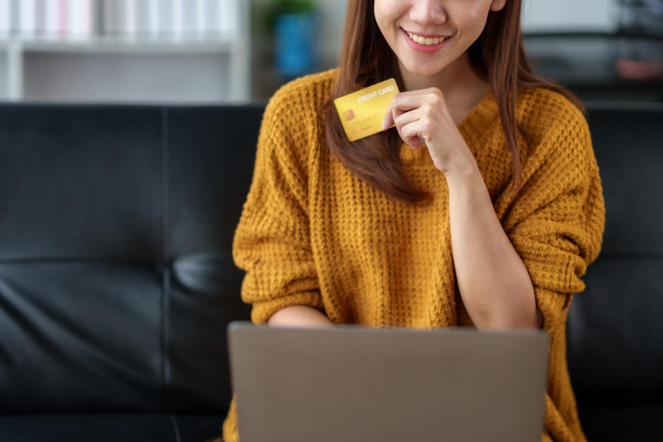 Asian woman using her laptop to shop online at home and pay bills with a credit card, illustrating a story on cashback cards.