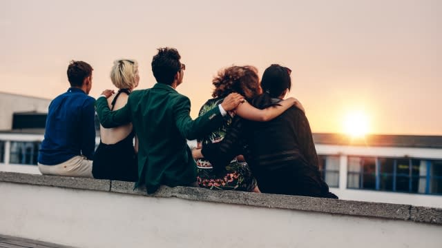 Friends sit on a ledge viewing the sunset.
