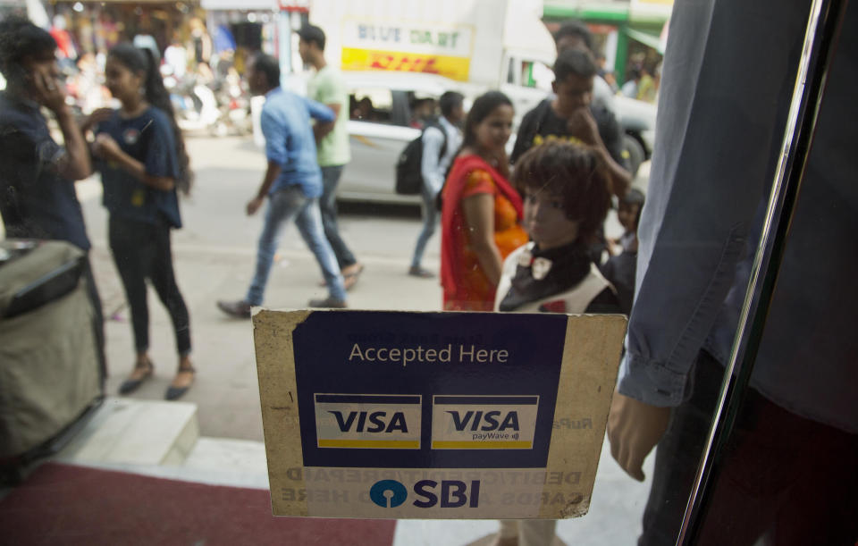 A VISA sticker is seen on the door of a shop in a market in Gauhati, India, Tuesday, Oct. 16, 2018. A customer uses a bank card to buy clothes inside a shop in Gauhati, India, Tuesday, Oct. 16, 2018. Global credit card and payments companies like American Express, Visa and MasterCard are facing a challenge in meeting a requirement to store transaction data for all Indian customers within the country. (AP Photo/Anupam Nath)