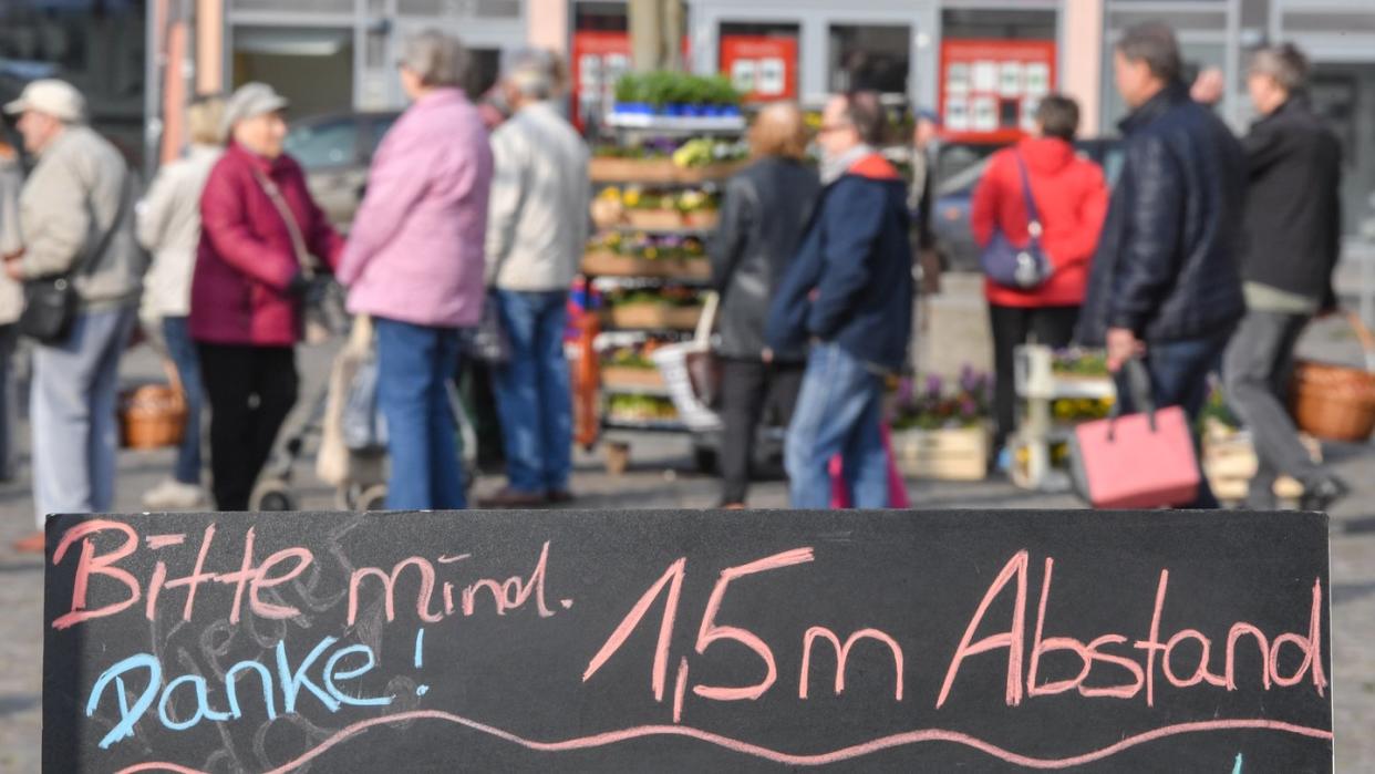 Ein Schild mit der Aufschrift «Bitte mind. 1,5m Abstand Danke!» steht auf einem Marktplatz.