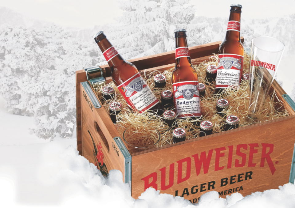 Bottles of Budweiser beer inside a crate that also has a few glasses.