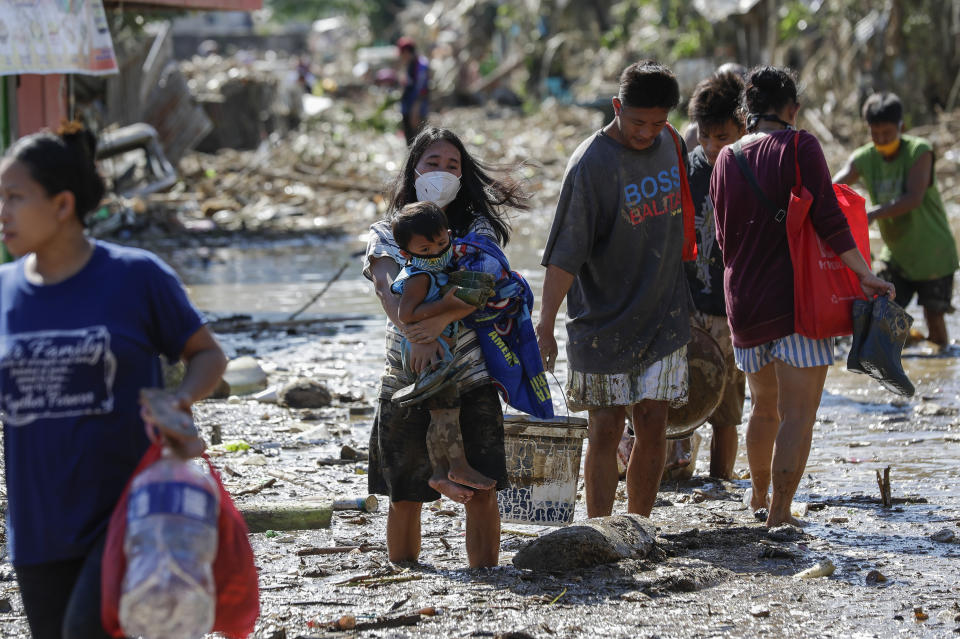 A woman carries her daughter through debris and floods in the typhoon-damaged Kasiglahan village in Rodriguez, Rizal province, Philippines on Friday, Nov. 13, 2020. Thick mud and debris coated many villages around the Philippine capital Friday after Typhoon Vamco caused extensive flooding that sent residents fleeing to their roofs and killing dozens of people. (AP Photo/Aaron Favila)