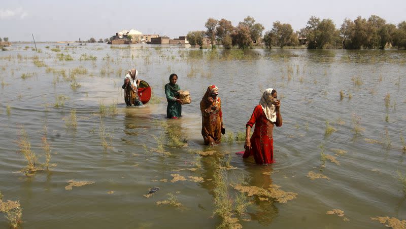 Pakistani women wade through floodwaters as they take refuge in Shikarpur district of Sindh Province, of Pakistan, Sept. 2, 2022. A major new United Nations report being released Monday, March 20, 2023, is expected to provide a sobering reminder that time is running out if humanity wants to avoid passing a dangerous global warming threshold.