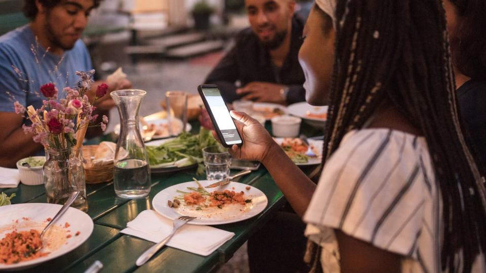 young woman using smart phone while having dinner with friends during garden party