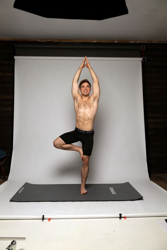 Julian Shaw does a yoga pose in front of a white screen