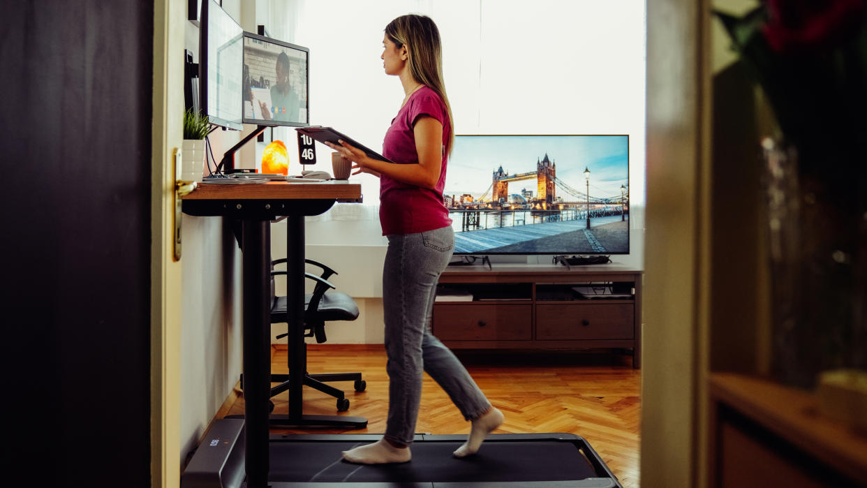  A woman on a walking treadmill working at an elevated desk. 