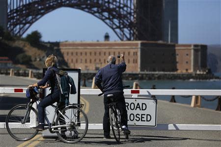 A bicyclist takes a photograph in front of the closed road gate to Fort Point National Historic Site, which has been closed due to the federal government shutdown, in San Francisco, California October 2, 2013. REUTERS/Stephen Lam