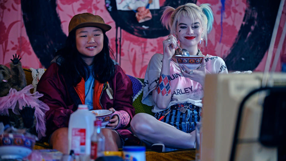 (L, R) Ella Jay Basco as Cassandra Cain and Margot Robbie as Harley Quinn, watching TV from a sofa, in Birds of Prey