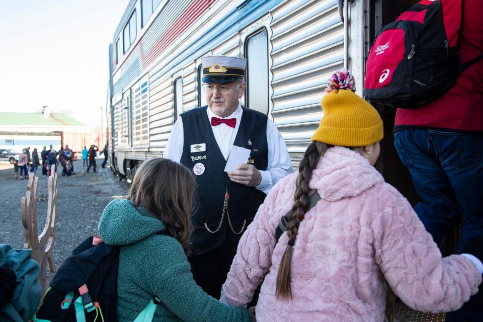 Volunteer car host Bruce Kuffer, of Lansing, checks passengers' tickets as he welcomes them abroad before the North Pole Express takes off in Owosso on Friday, Nov. 24, 2023.