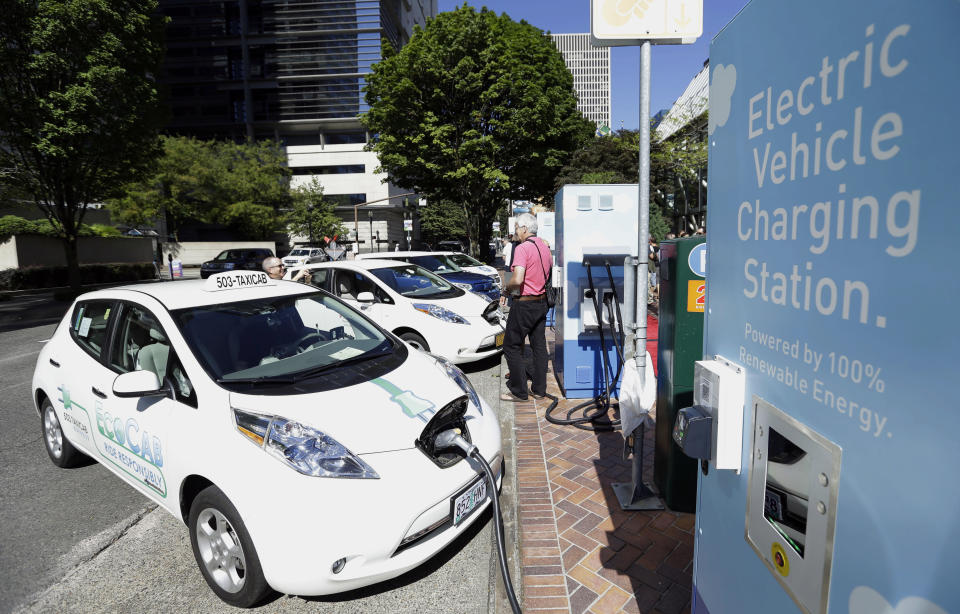 FILE - A line of electric cars and newly installed charging stations sit in front of the Portland General Electric headquarters building on July 28, 2015, in Portland, Ore. Oregon will temporarily suspend rebates for buying or leasing an electric vehicle for a year starting in May. The Oregonian/OregonLive reports the suspension comes because too many people are applying and the program is running out of money. (AP Photo/Don Ryan, File)