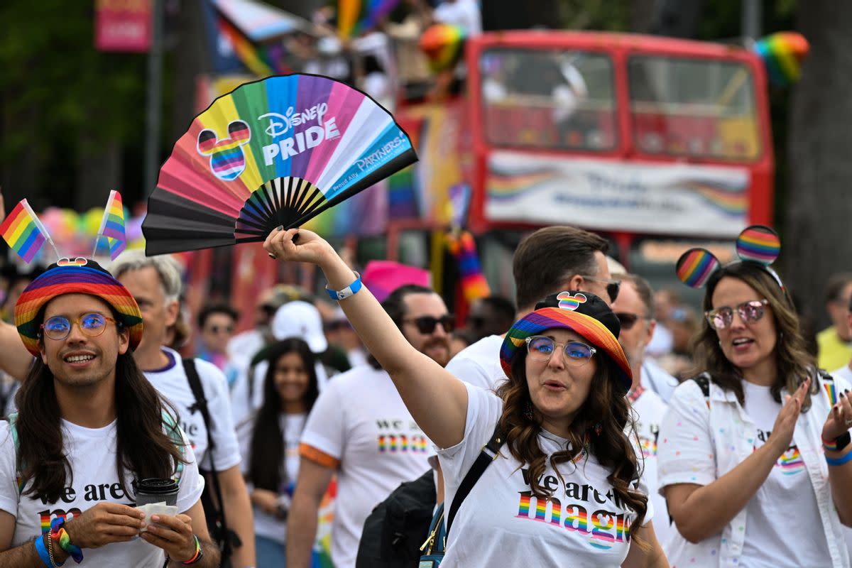 A person holds a fan that says Disney PRIDE on it. They are sounded by other people in a crowd. All the people in the photo appear to be wearing "we are magic" shirts, with the magic have rainbow colors in it. ROBYN BECK/AFP via Getty Images