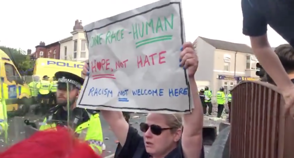 A woman held up a placard in front of rioters in Southport. (X/Liverpool Post)