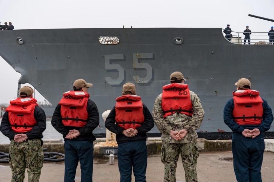 Sailors wearing lifevests hold their hands behind their backs as they observe the guided-missile cruiser USS Leyte Gulf depart Naval Station Norfolk.