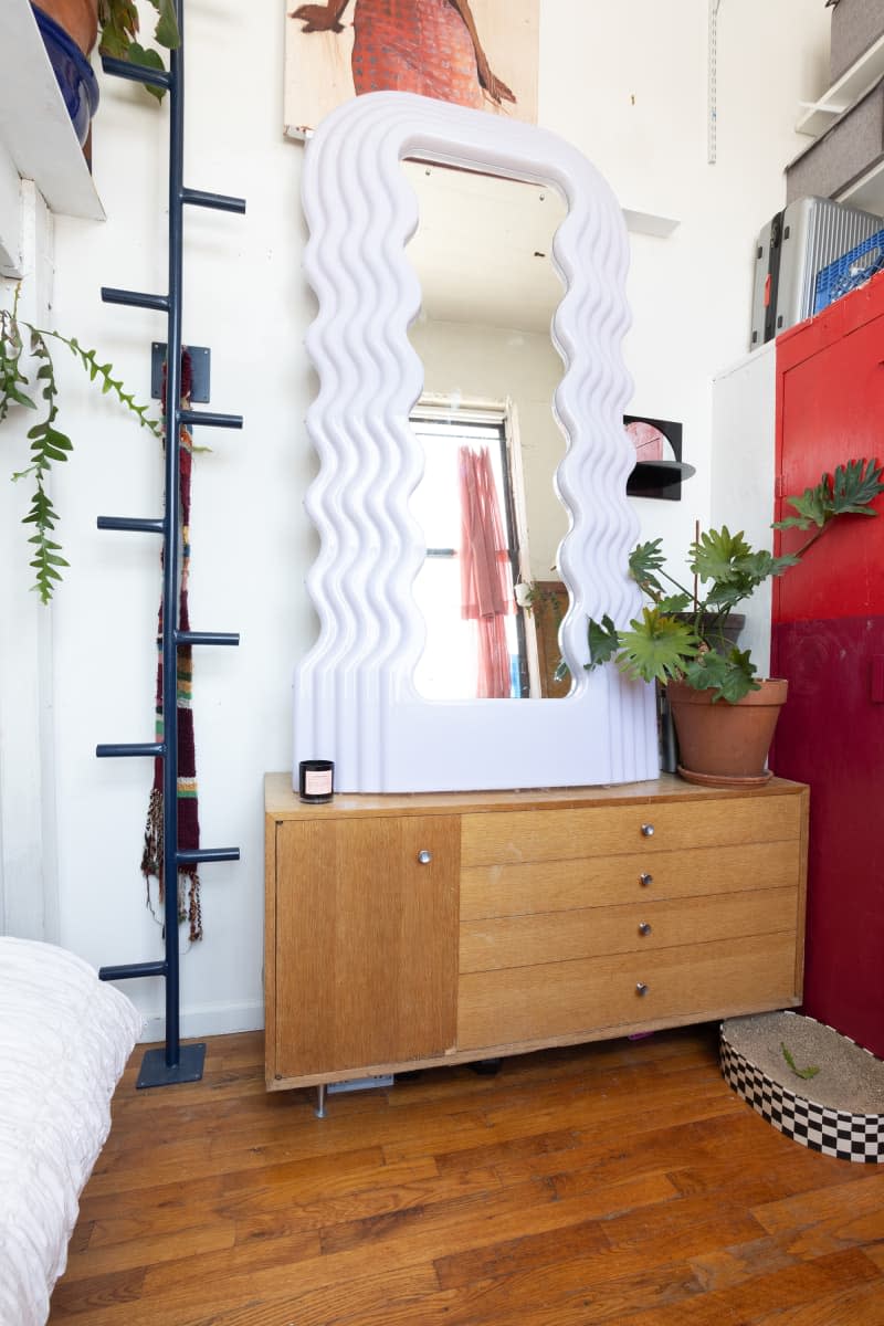 Wavy floor mirror mounted on top of wooden dresser in eclectic bedroom.