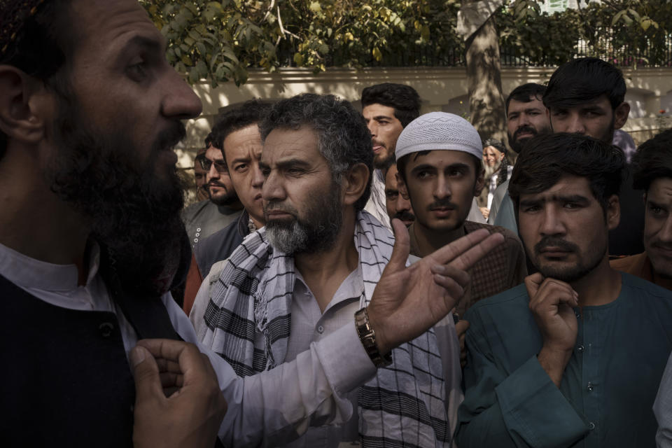 A member of the Taliban, left, talks to Afghans gathering outside a government passport office recently re-opened after Taliban announced they would be issuing a backlog of applications approved by the previous administration in Kabul, Afghanistan, Wednesday, Oct. 6, 2021. (AP Photo/Felipe Dana)