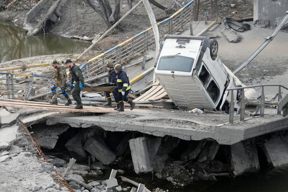 Ukrainian soldiers carry a body of a civilian killed by the Russian forces over the destroyed bridge in Irpin close to Kyiv, Ukraine, Thursday, March 31, 2022. The more than month-old war has killed thousands and driven more than 10 million Ukrainians from their homes including almost 4 million from their country. (AP Photo/Efrem Lukatsky) ORG XMIT: XEL115