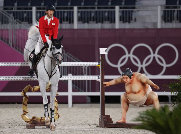 A rider clears the barrier as the statue of a sumo wrestler looks in the Tokyo Olympics equestrian competition. ) (Photo: picture alliance via Getty Images)