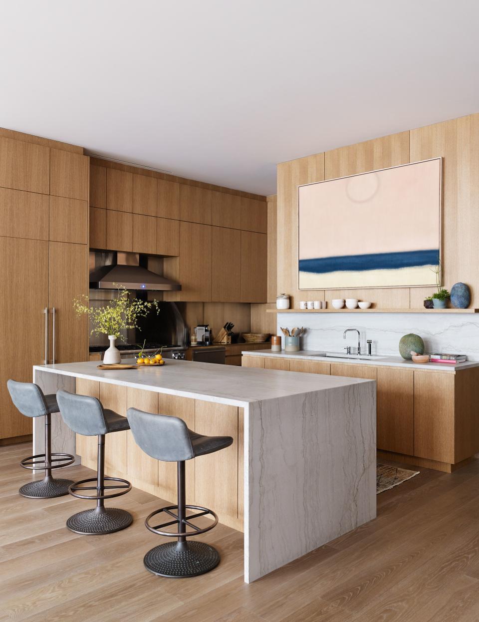 The custom kitchen cleverly marks the transition between the public and private spaces, and features an oversized quartzite island. The stools are by Ilmari Tapiovaara from Dual Modern. The painting is by Susan Vecsey.