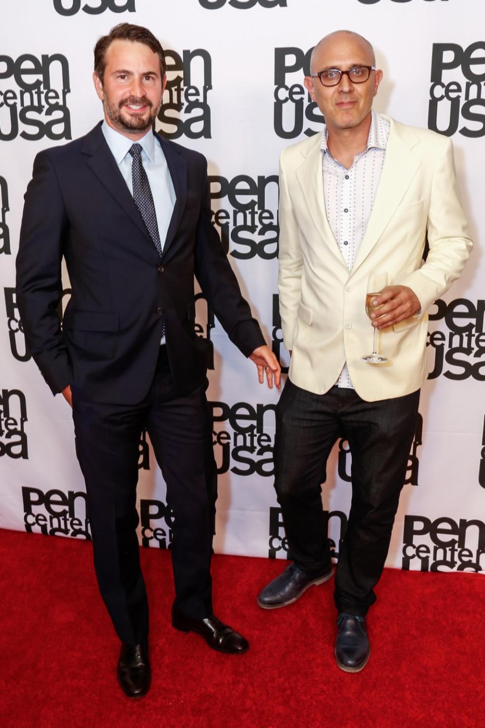 A man in a suit, left, and a man in a white sport coat on a red carpet