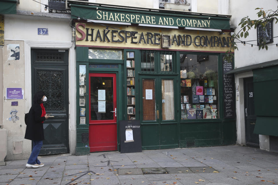 A woman walks by the closed English and American literature Shakespeare bookstore in Paris, Tuesday, Nov.3, 2020. French supermarkets are banned from selling flowers and books but they can still sell baby care products, according to a decree published Tuesday laying out new rules for what are considered "essential" items during a monthlong lockdown effort to slow virus infections and save lives. Supermarkets are sealing off aisles or taking products off shelves based on the new rules, which came after small businesses like florists and bookstores complained that they were being unfairly punished because they were forced to close down. (AP Photo/Michel Euler)