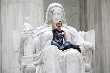 A protester sits on the lap of "Lady Justice" on the steps of the U.S. Supreme Court building as demonstrators storm the steps and doors of the Supreme Court while Judge Brett Kavanaugh is being sworn in as an Associate Justice of the court inside on Capitol Hill in Washington, U.S., October 6, 2018. REUTERS/Jonathan Ernst