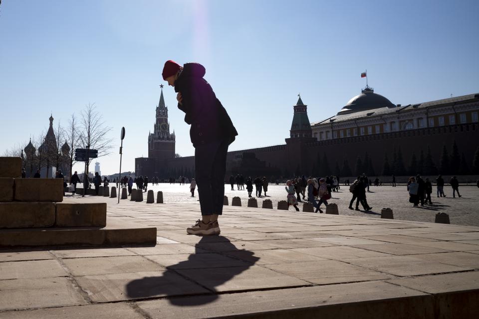 A woman crosses herself in front of Church of Our Lady of Kazan in Red Square with the St. Basil's Cathedral, left, and the Spasskaya Tower, second left, and the Kremlin Wall in the background, in Moscow, Russia, Sunday, March 20, 2022. (AP Photo)