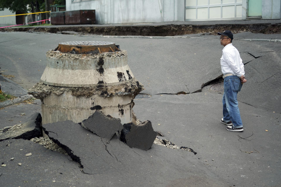 FILE - In this Sept. 7, 2018, file photo, a neighbor walks by a manhole where the ground sank by an earthquake in Kiyota, outskirts of Sapporo city, Hokkaido, northern Japan. A magnitude 6.7 earthquake on Japan’s northernmost main island on Sept. 6 killed 41 people, most of them buried in a massive landslide. It wrecked roads and houses in the regional capital, Sapporo, and triggered a region-wide power outage. Local media cited Hokkaido Gov. Harumi Takahashi as saying the cost to public infrastructure, farming and forestry was estimated at 150 billion yen ($1.3 billion), not including losses to tourism and private businesses. (AP Photo/Eugene Hoshiko, File)