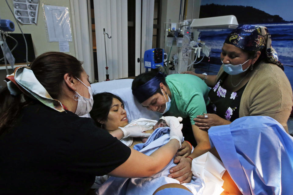 A midwife, left, tends to Angela Quintana Aucapan and her newborn son, Namunkura, as the child’s father, Cristian Fernandez Ancapan, and Ingrid Naipallan, a machi, or spiritual guide, accompany them at the San Jose de Osorno Base Hospital in Osorno, Chile, Saturday, Aug. 20, 2022. The largest public hospital in Osorno is finding new ways to incorporate Indigenous health care practices, such as having a machi help with delivery. (AP Photo/Luis Hidalgo)