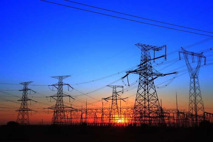 Rows of power transmission lines and transformers near sunset or sunrise.