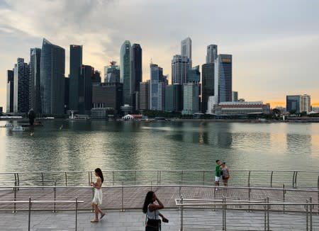 Passers-by hold their mobile phones as people take a selfie photo using a smartphone, with Singapore's central business district skyline, in Singapore