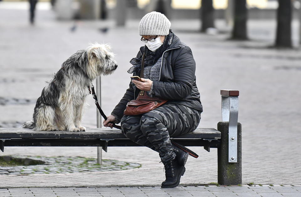 A woman with a face mask and a dog sit on a bench at the almost abandoned downtown in Duisburg, Germany, Monday, Jan. 25, 2021. (AP Photo/Martin Meissner)