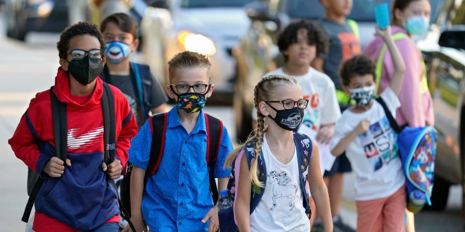 A group of kids wearing masks and backpacks walk toward their classrooms.