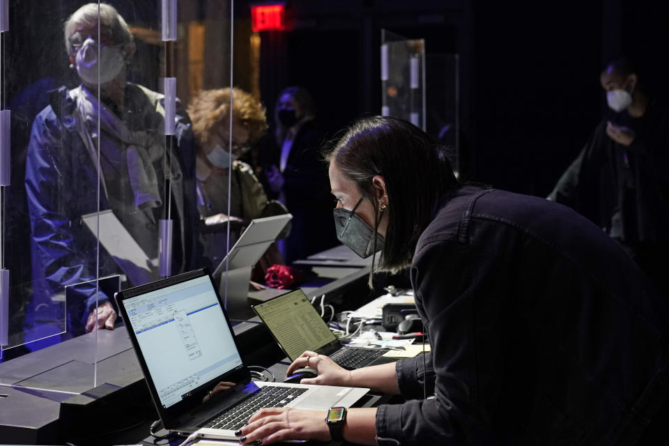 Concertgoers are protected behind plastic protectors as an employee checks her computer for their reservations before the start of a performance by the New York Philharmonic at The Shed in Hudson Yards, Wednesday, April 14, 2021, in New York. It was the first time the Philharmonic had performed together for a live audience since March 10, 2020. (AP Photo/Kathy Willens)
