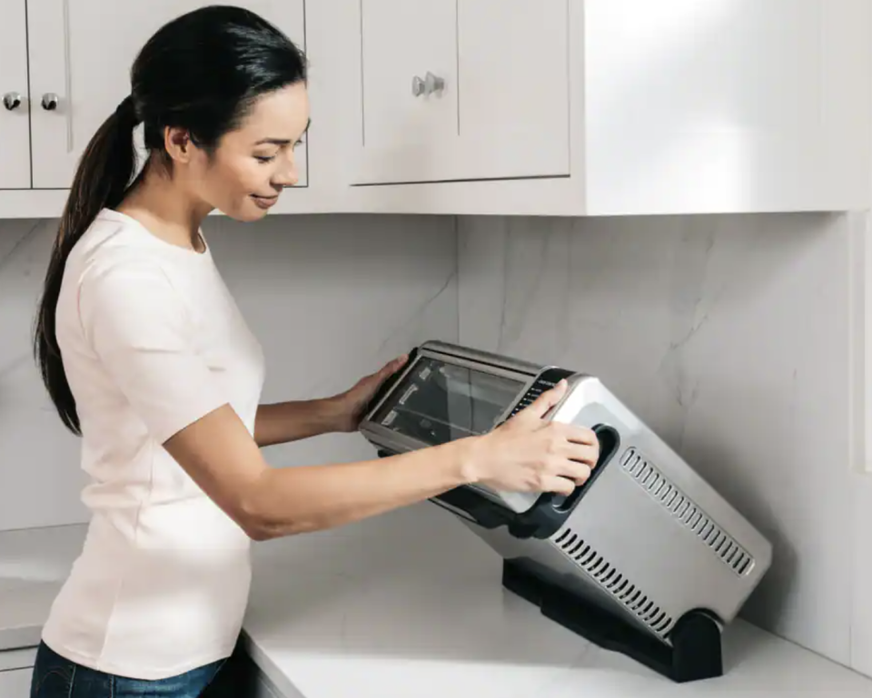 woman holding Ninja Foodi 8-in-1 Digital Air Fryer Toaster Oven on kitchen countertop (Photo via Canadian Tire)