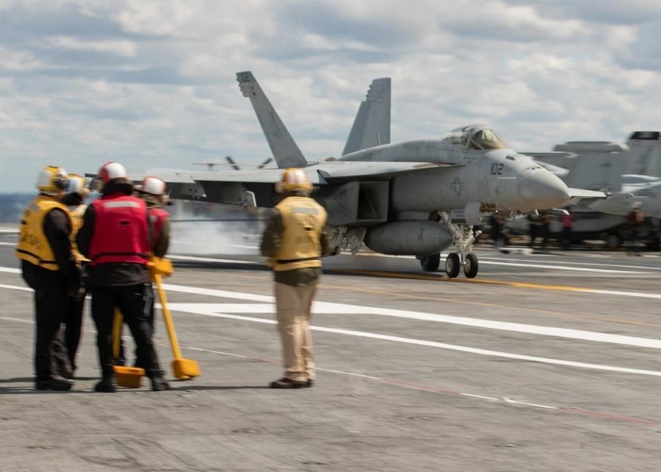 a fighter jet lands on the flight deck of a military aircraft carrier