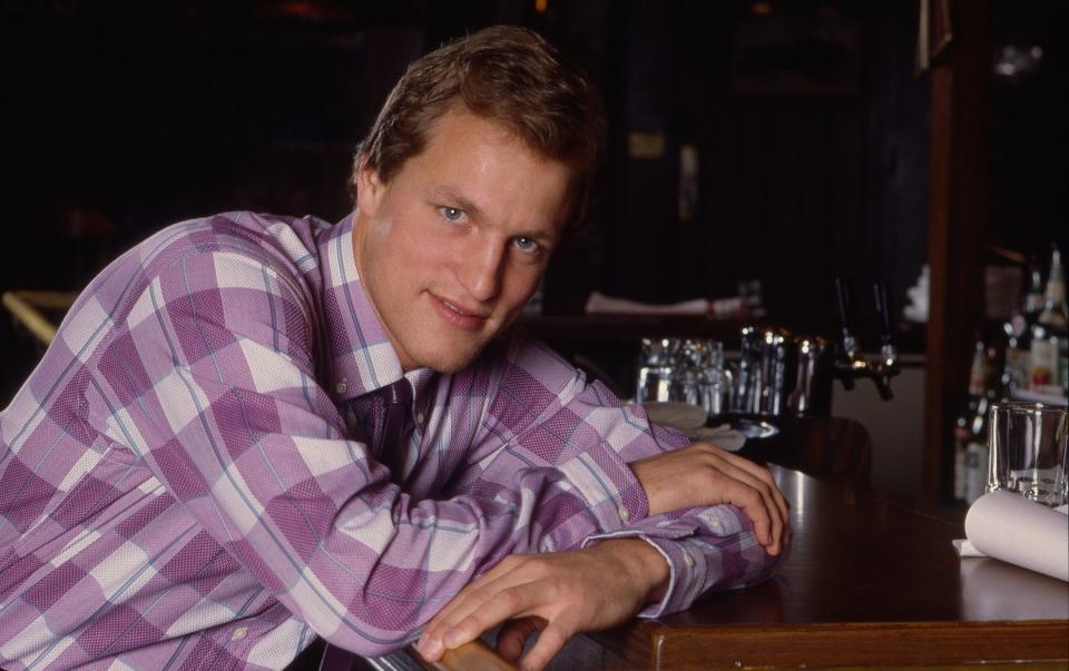 Woody Harrelson dressed in a purple plaid shirt while appearing as Woody Boyd on the set of "Cheers."