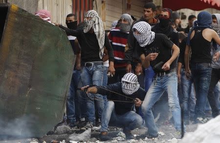 A masked Palestinian protester uses a slingshot to throw stones at Israeli troops as others take cover during clashes in the West Bank city of Hebron October 9, 2015. REUTERS/Mussa Qawasma