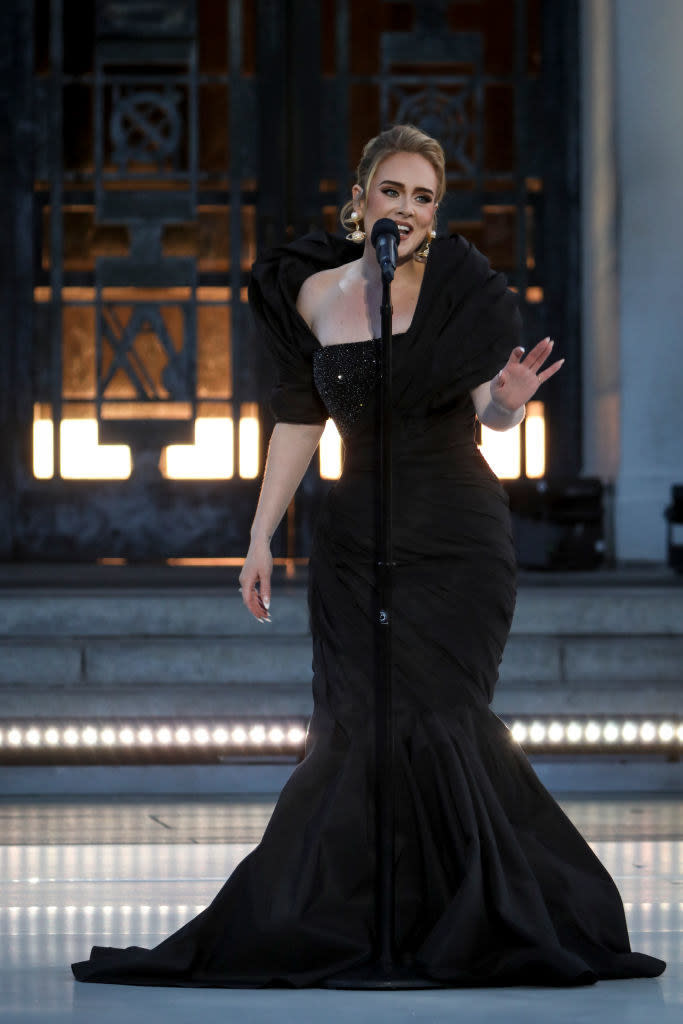 Adele performing onstage at her concert special; she's wearing an Old Hollywood–inspired black gown