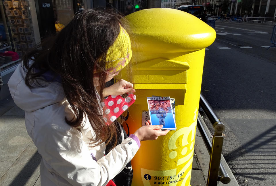 Madrid, Spain - December 13, 2016: Woman drops postcard in a street postbox of Correos, the national postal service of Spain.