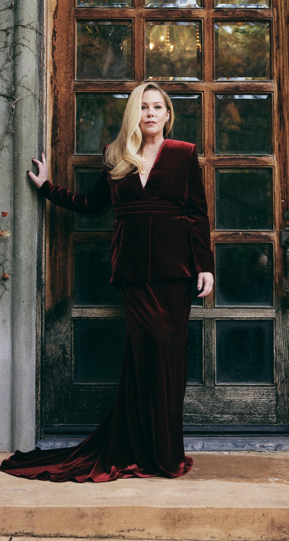 Christina stands at a doorway in an elegant velvet dress with a trailing skirt