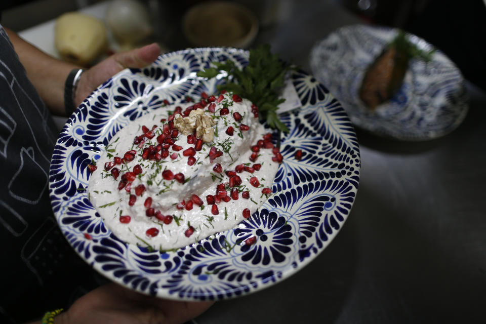 In this Sept. 13, 2019 photo, a cook carries out finished chiles en nogada to be served to diners at Testal restaurant in downtown Mexico City. Testal has dedicated nearly an entire kitchen to the production of the emblematic dish, selling around 150 chiles per day, and attempting to more than double the 3000 chiles they sold last year during the short season. (AP Photo/Rebecca Blackwell)