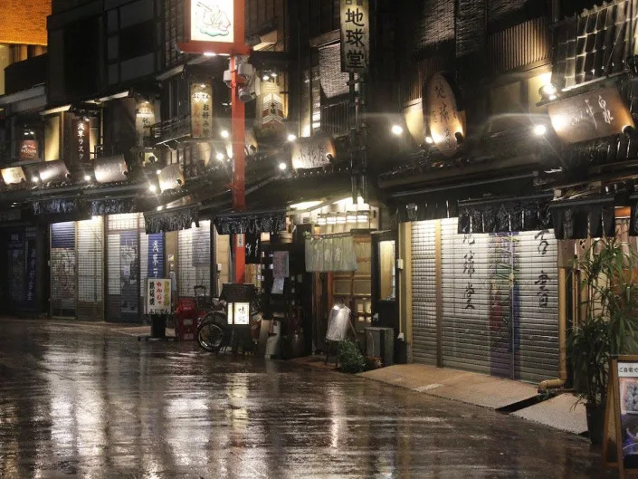 tokyo street at night with rainy sidewalk, shops to the right