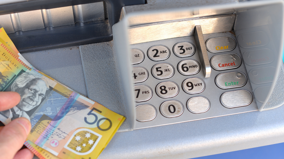 A person holds $50 notes while using an ATM at a bank.