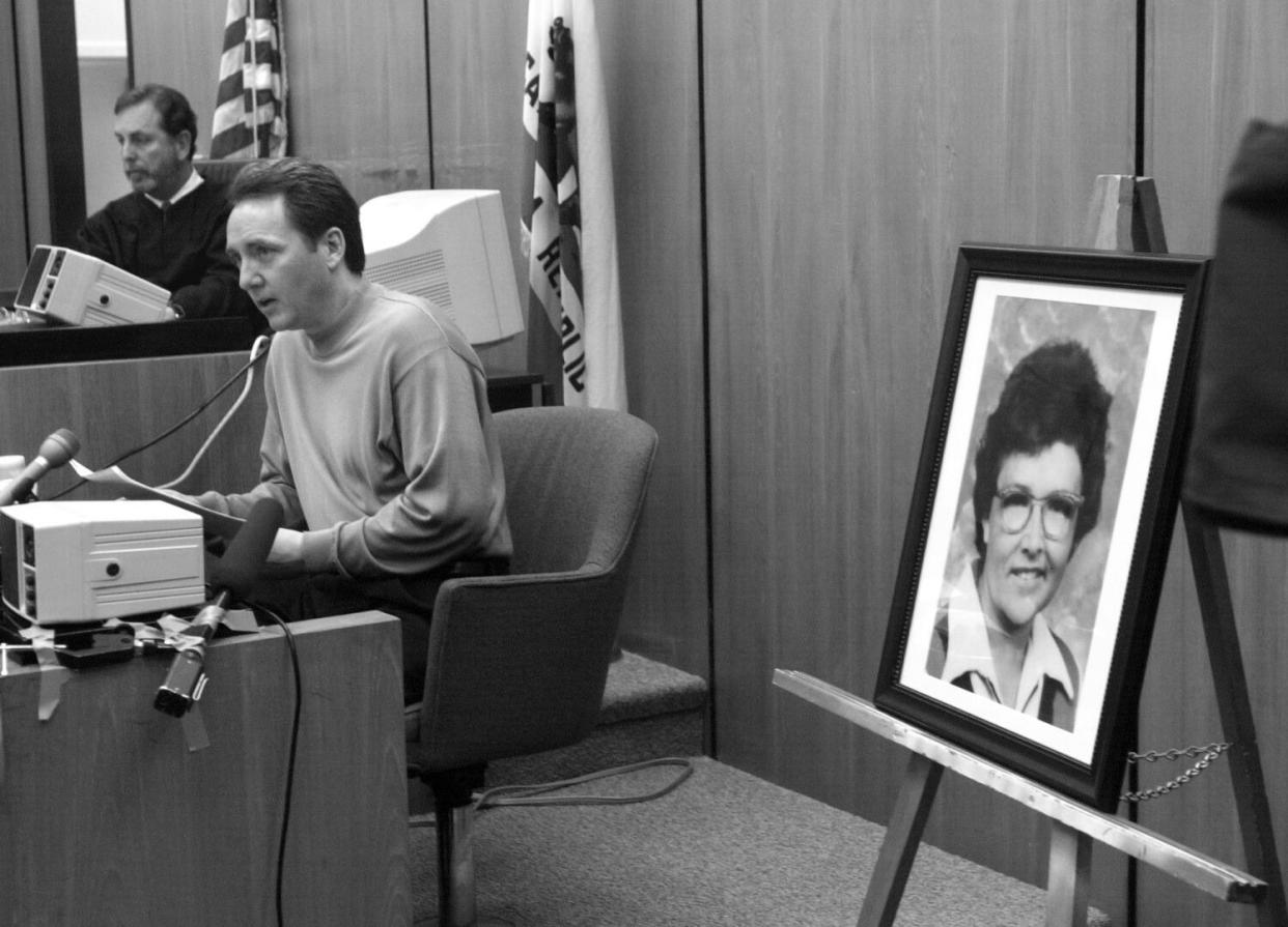 A man speaks in court next to a woman's portrait on an easel