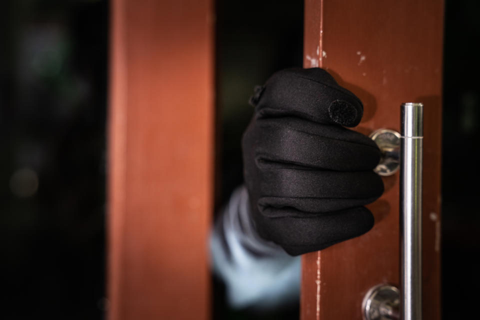 dangerous masked burglar with crowbar breaking into a victim's home door