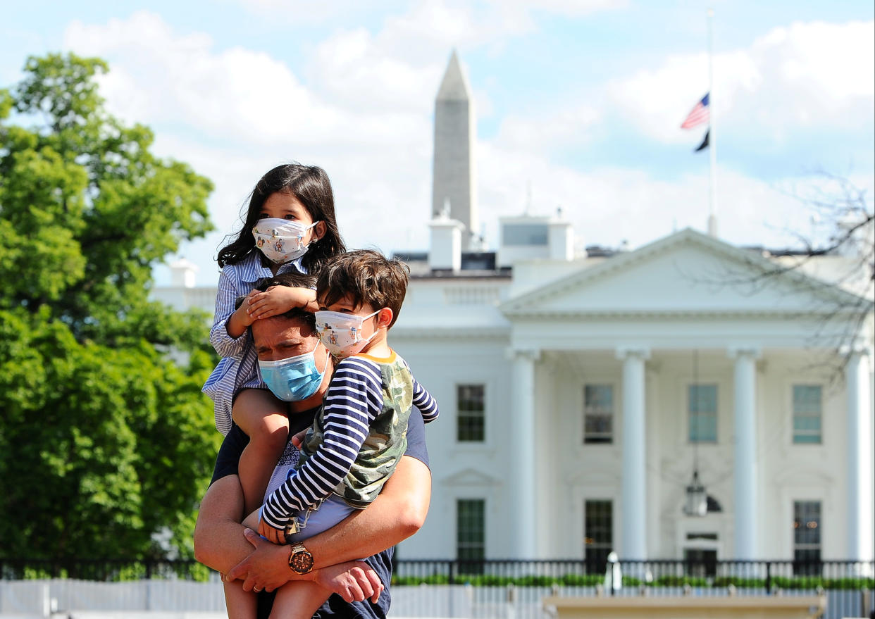 Jason Aguirre carries his children, Elle, 4, and Shai, 6, after viewing the White House, where flags fly at half-staff to commemorate the victims of the coronavirus disease (COVID-19), in Washington, U.S., May 23, 2020. REUTERS/Mary F. Calvert     TPX IMAGES OF THE DAY