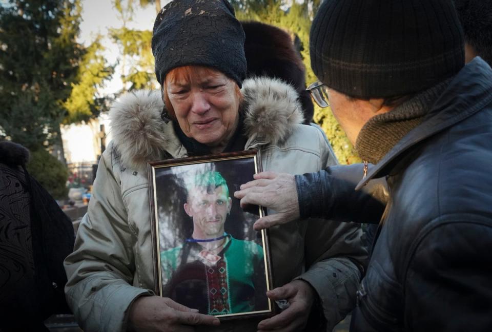 The mother of Ukrainian children’s writer Volodymyr Vakulenko holds his photo near his grave in Kharkiv on Tuesday (AP)