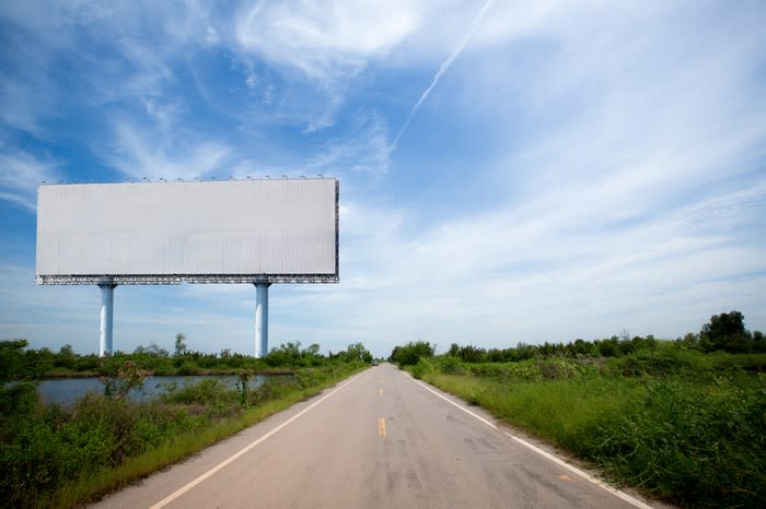 Blank billboard next to a clear country highway.