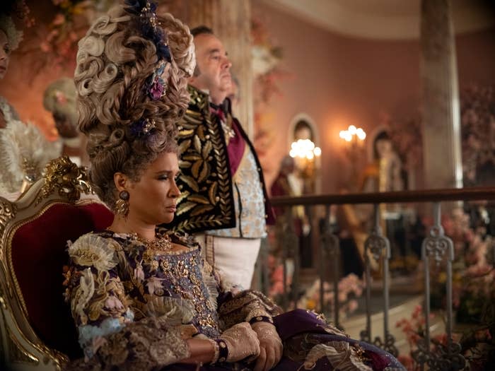 Golda Rosheuvel and Hugh Sachs in elaborate period costumes with intricate embroidery, seated and standing respectively